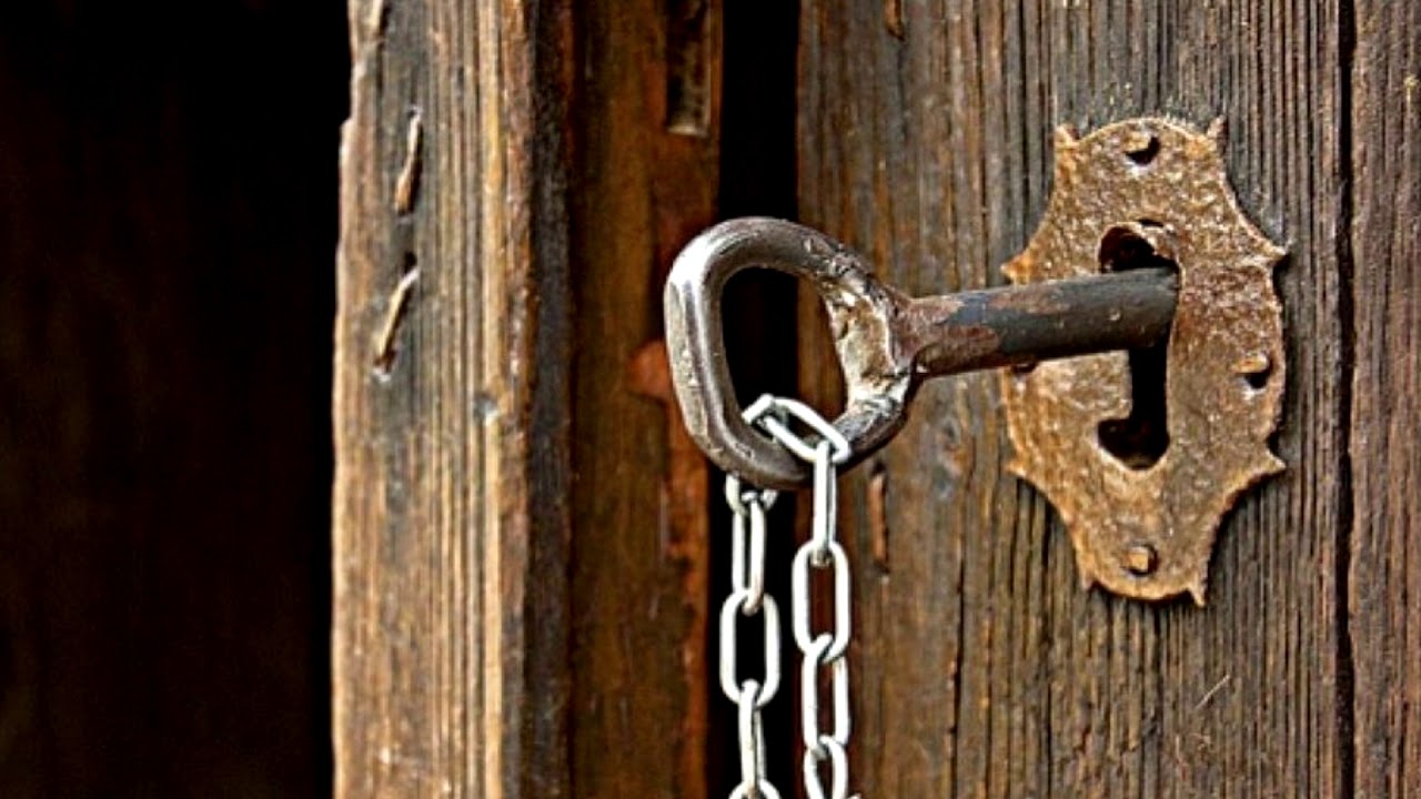 Una llave de hierro antigua insertada en una cerradura de madera desgastada, con una cadena colgando de la llave.